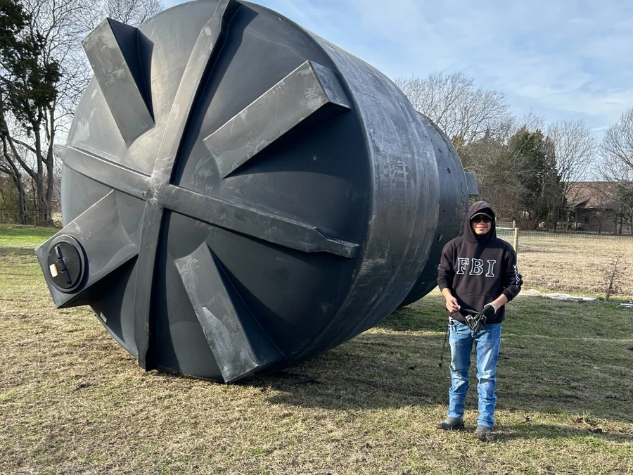 Large-capacity Eco Water Solutions rainwater harvesting storage tank installed at a Texas property, shown at scale beside a crew member